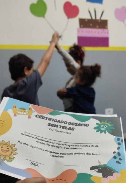 Certificado “Desafio sem telas” impresso, com crianças brincando ao fundo.